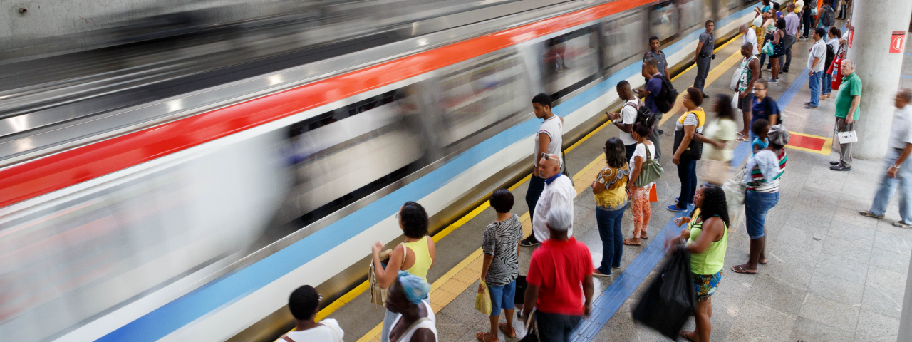 Passageiros aguardando na plataforma enquanto trem se aproxima em estacão de metrô movimentada.