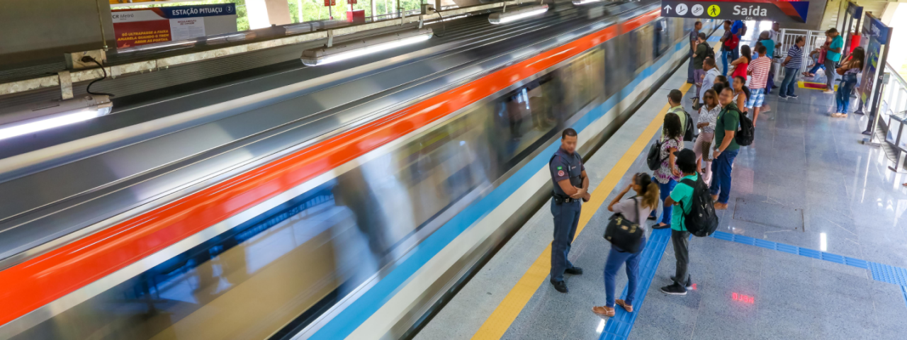 Imagem da Estação Pituaçu, localizada na Avenida Paralela mostra a imagem de um trem em movimento com alguns usuários na plataforma.