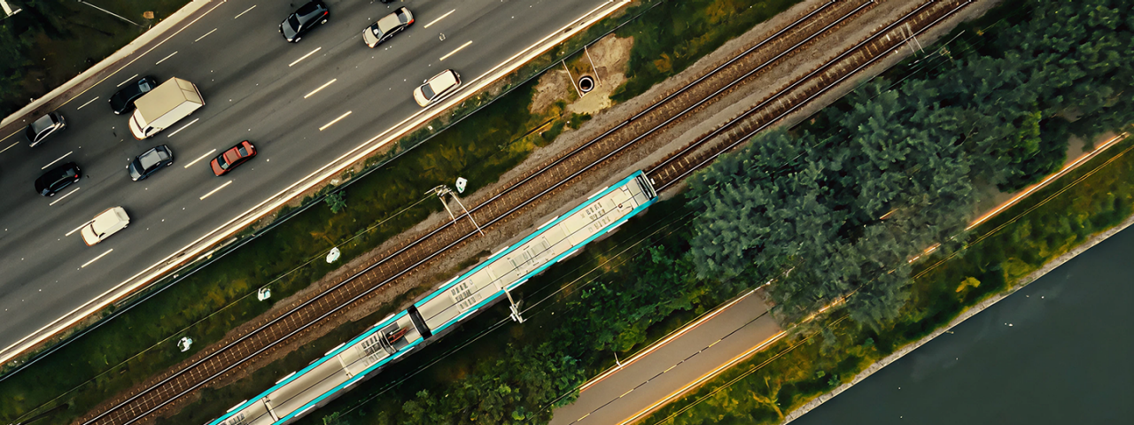 Vista aérea da linha metroferroviária da Motiva Trilhos ao lado de via expressa, com trem em circulação e faixa de domínio delimitada por áreas verdes
