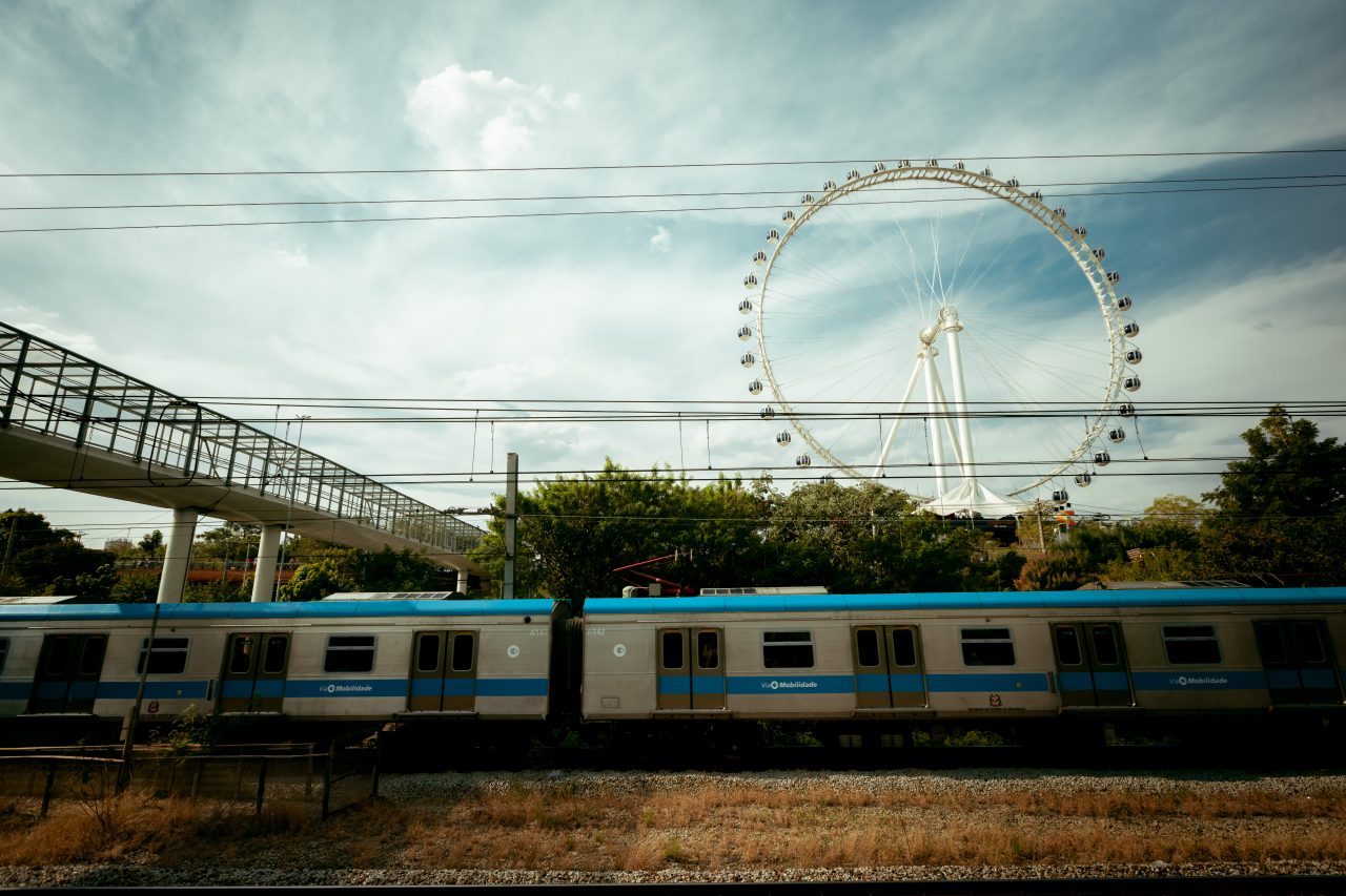 Trem da Linha 9-Esmeralda em circulação com a Roda-Gigante de São Paulo ao fundo no Parque Villa-Lobos.