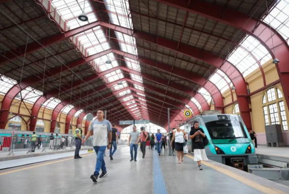 Interior histórico restaurado da Estação Júlio Prestes, com estrutura metálica vermelha e movimento de passageiros