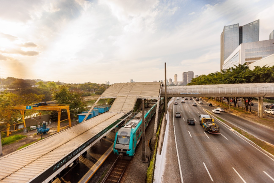 Estação sustentável da ViaMobilidade com trem parado ao lado de via expressa, skyline de São Paulo ao fundo