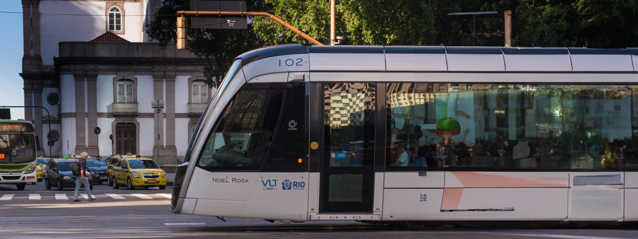VLT do Rio de Janeiro, modelo Noel Rosa, circulando pelo centro da cidade, com pedestres atravessando e trânsito ao fundo.