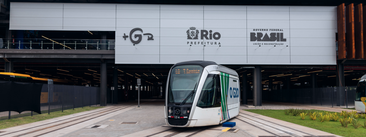VLT do Rio de Janeiro parado em frente à estação com logos da Prefeitura do Rio e Governo Federal visíveis na fachada.